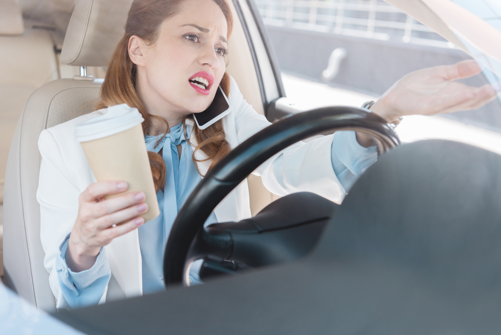 Distracted woman driving while talking on the phone and drinking coffee